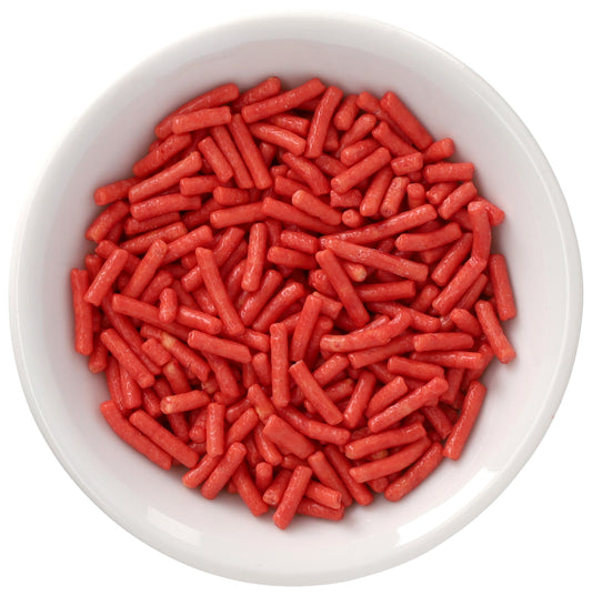 White bowl filled with soft red Natural Dyed Made Simply™ rod-shaped sprinkles, shown in a close-up overhead view on a white background.