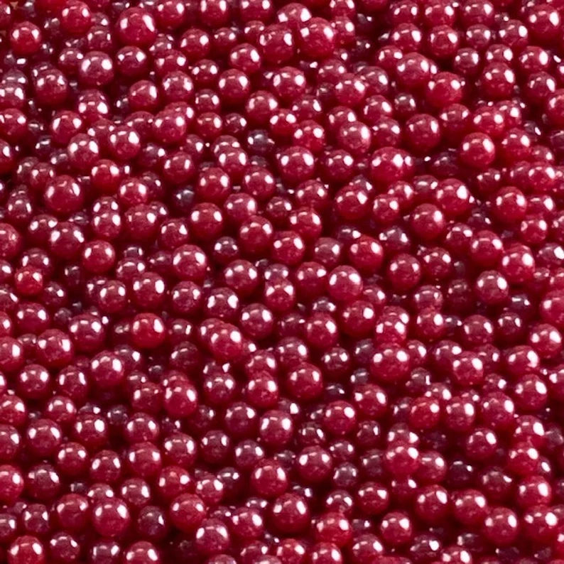 Close-up of glossy red pearlized edible dragees, 4mm round sugar pearls with a smooth reflective shine; red cake sprinkles for decorating cupcakes, cookies, and cakes.