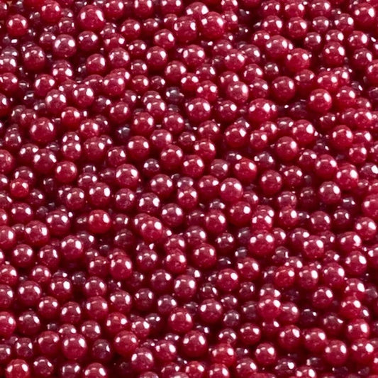 Close-up of glossy red pearlized edible dragees, 4mm round sugar pearls with a smooth reflective shine; red cake sprinkles for decorating cupcakes, cookies, and cakes.