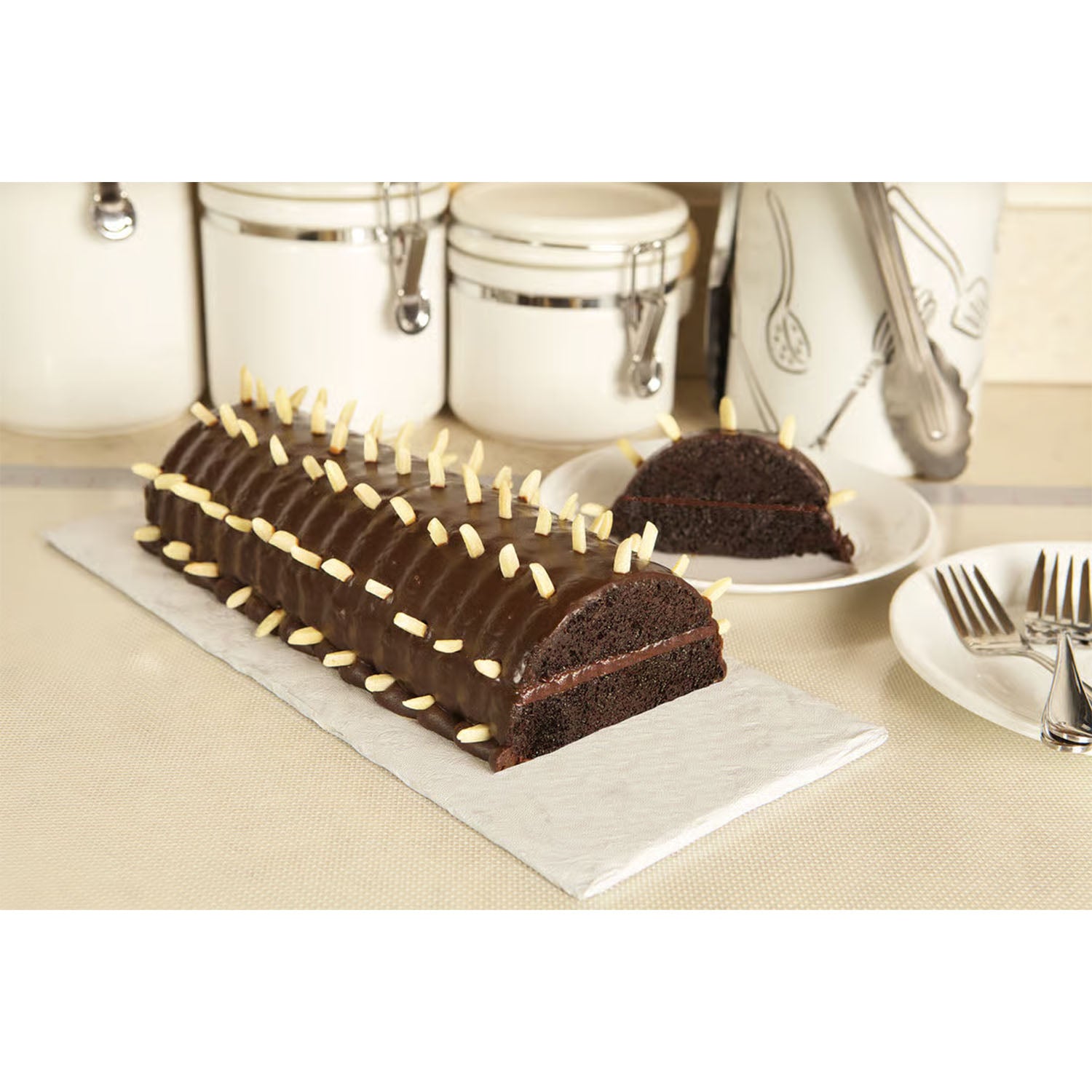 Chocolate Rehrücken cake topped with slivered almonds and sliced to show interior texture, displayed on a white board in a kitchen setting.
