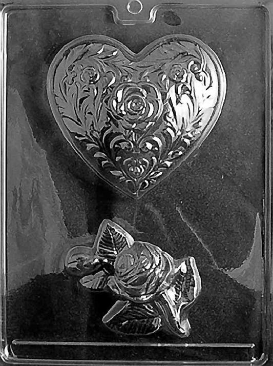 Chocolate mold with two cavities: one heart-shaped mold embossed with detailed roses and floral scrollwork, and one three-dimensional rose corsage mold with layered petals and leaves, displayed on a dark background.