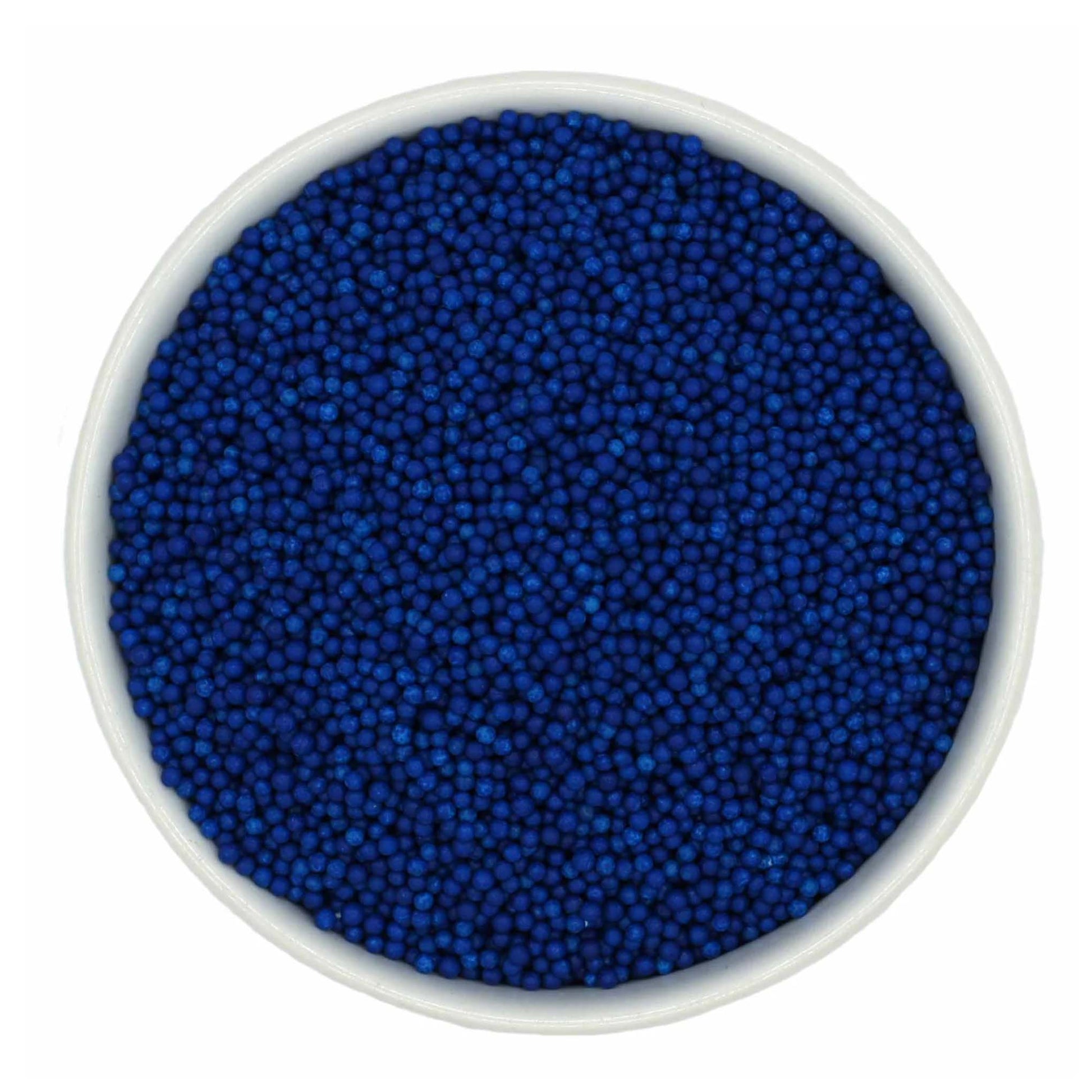 Top-down view of a white bowl filled with royal blue non-pareils, showing tiny round sprinkle beads in a deep vivid blue shade.