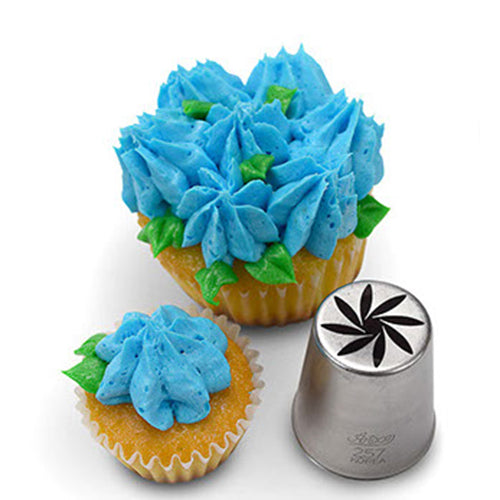 A Russian piping tip next to two cupcakes decorated with blue star-shaped buttercream flowers and green leaves, showcasing the detailed star flower designs made by the tip.