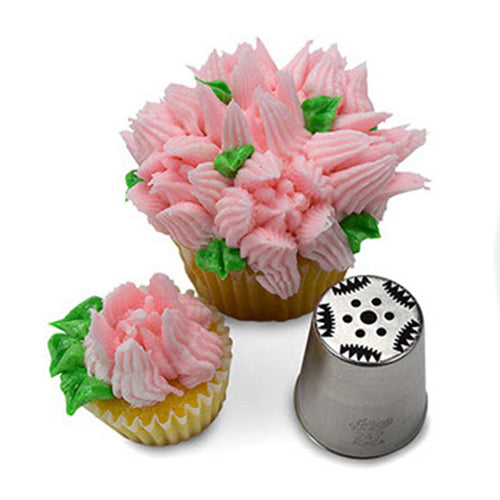 Cupcake decorated with intricate white and pink frosting flowers and green leaves, made using Russian Piping Tip #247. The corresponding metal piping tip is shown beside the cupcake, highlighting its precise pattern.