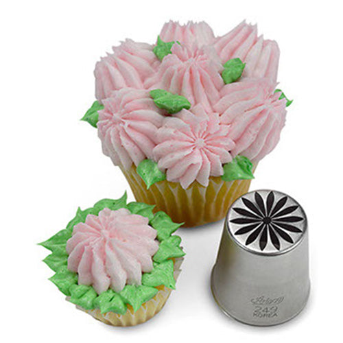 A Russian piping tip next to two cupcakes, each decorated with pink buttercream flowers and green leaves, demonstrating the multi-petal floral designs the tip creates.