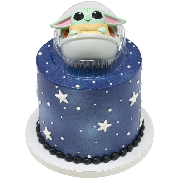 Tall round navy blue cake with white star decorations and dotted “galaxy” pattern, topped with Grogu in a Hover Pram inside a clear plastic display tray.