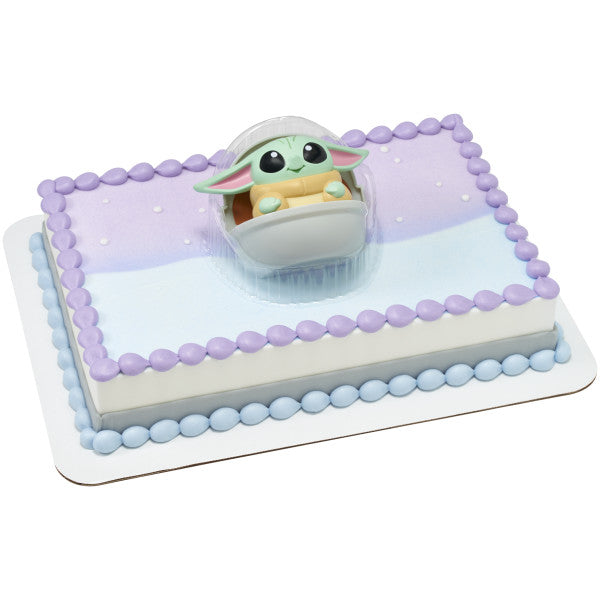 Rectangular sheet cake with lavender and light blue icing, piped purple and blue bead borders, and Grogu in a Hover Pram displayed in a clear plastic tray at the center.