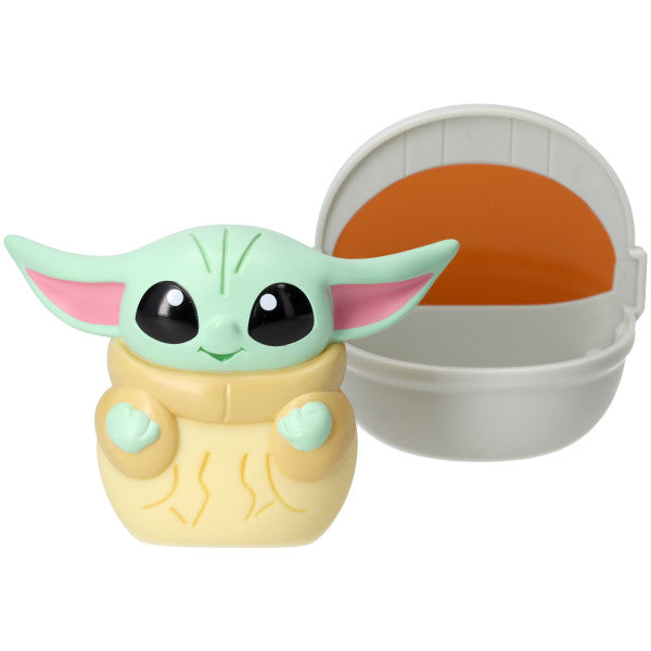 Squishy Grogu cake topper figure with mint green head, large black eyes, and beige robe next to a gray Hover Pram with orange interior, shown on a white background.
