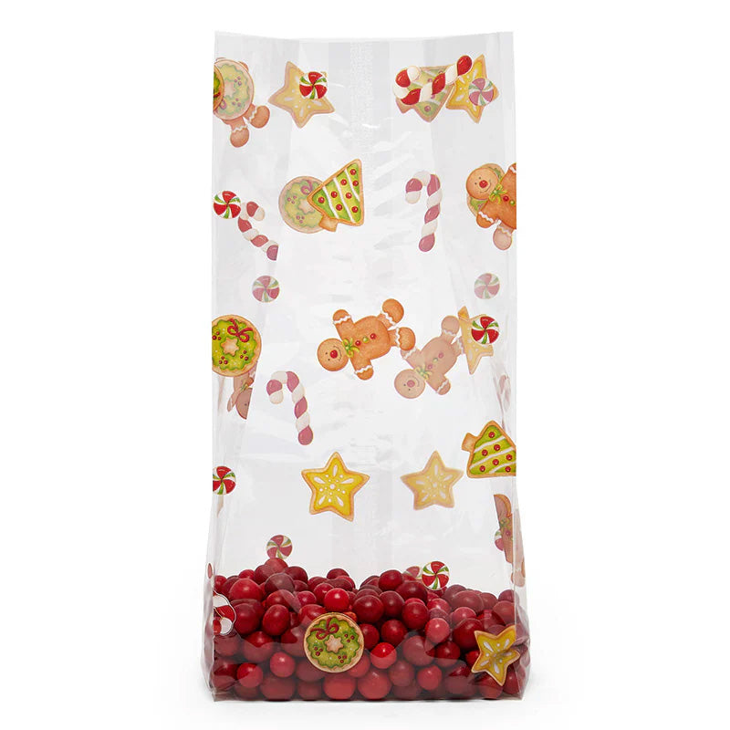 Clear large gusseted cellophane treat bag printed with cartoon candy canes, gingerbread men, star cookies, and Christmas tree cookies, shown upright with red candy pieces at the bottom.