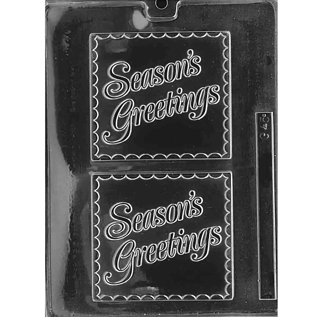 Clear plastic chocolate mold with two large square cavities, each embossed with “Season’s Greetings” in flowing script and a scalloped border; shown on a dark background.
