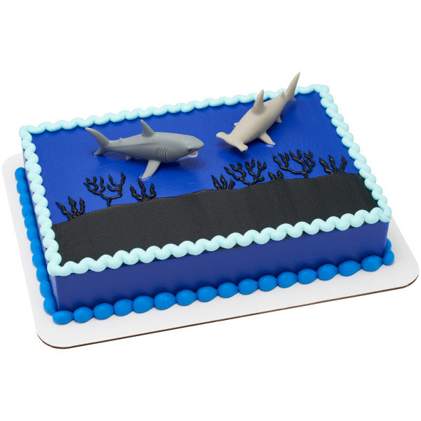 A rectangular ocean-themed cake with a deep blue design, topped with the Shark Attack DecoSet featuring two shark figurines.