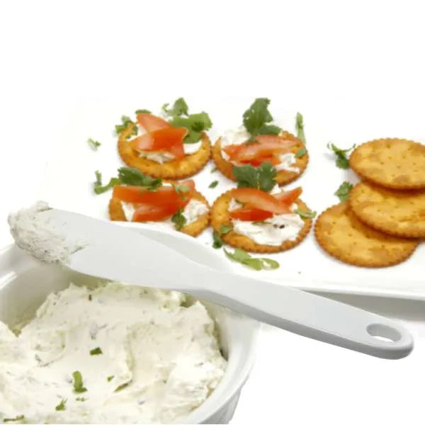 Small spatula used to spread cream cheese on crackers with tomato and herbs.