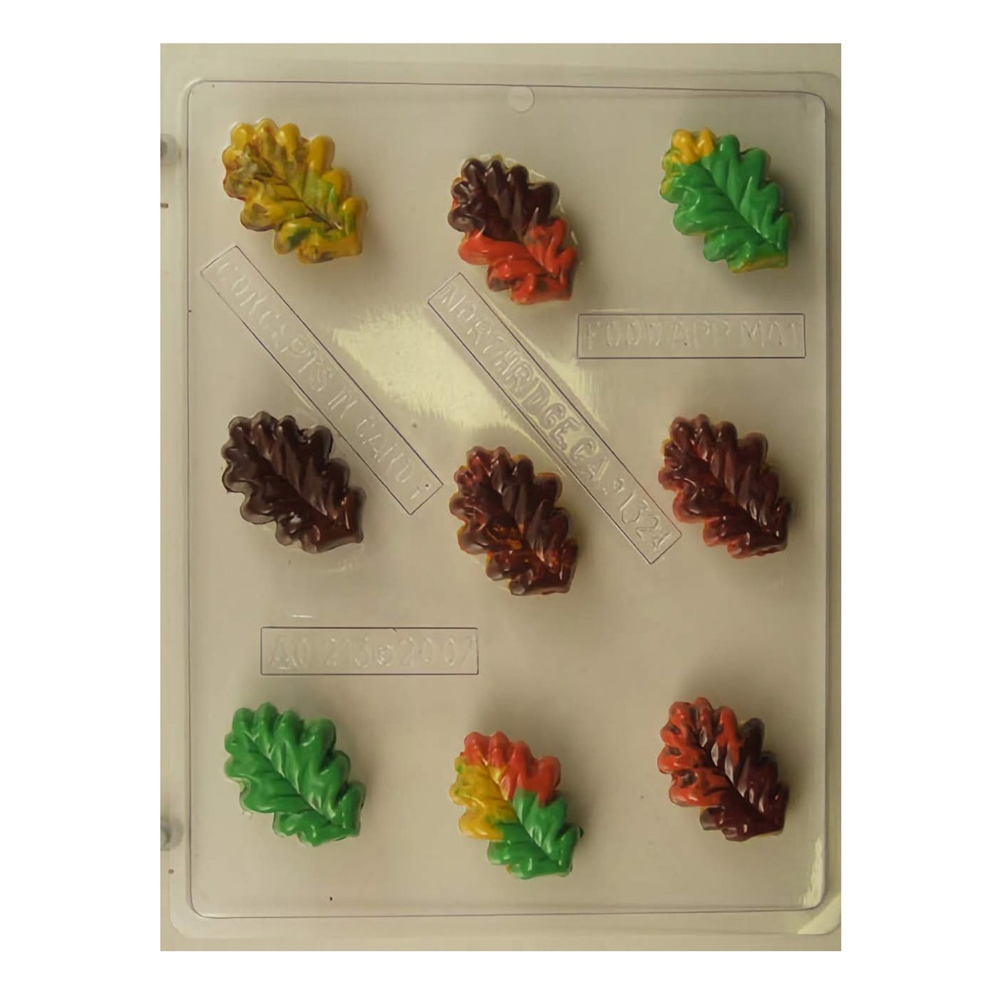 Chocolate mold sheet for creating small oak leaf-shaped confections, with multiple cavities displaying intricately detailed veins of the leaves. The mold includes finished examples in autumnal colors such as yellow, green, red, and brown, emphasizing the seasonal theme of the mold suitable for fall festivities and decorations.