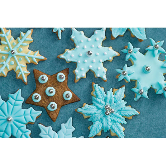 Assorted decorated snowflake cookies in blue and white icing made using plunger cutters, displayed on a dark blue background.