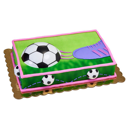 Vibrant soccer ball cake, featuring a black and white soccer ball half-embedded in green icing with grass details and a pink border. Ideal for soccer fans and sports-themed parties.