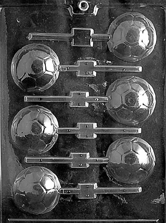 Clear lollipop mold with six soccer ball cavities featuring hexagon and pentagon panel details, each with built-in stick channels on a glossy plastic sheet.