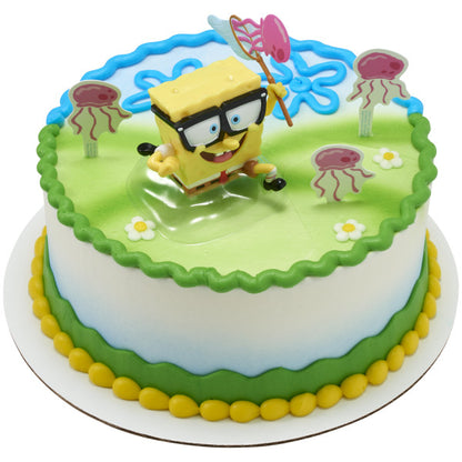Round cake with green and blue icing bands and a yellow border, topped with SpongeBob holding a jellyfish net on a clear base and pink jellyfish pick toppers placed around the top.
