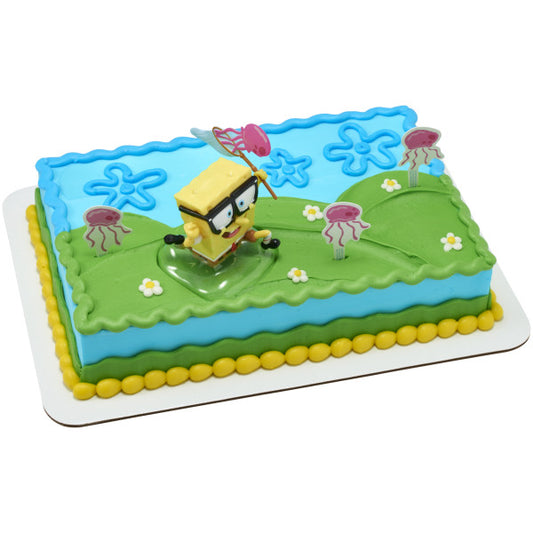 Rectangular cake decorated like Jellyfish Fields with blue and green icing, flower shapes piped on top, SpongeBob topper on a clear base, and pink jellyfish picks spaced around the scene.