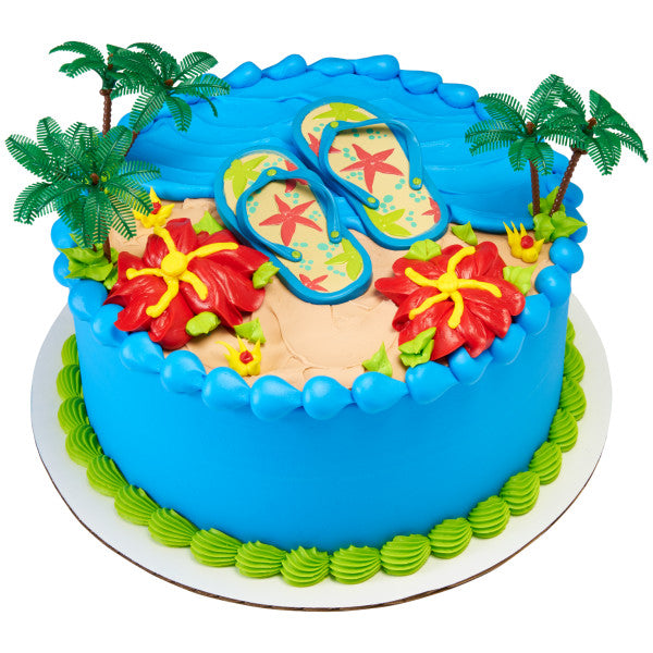 A round cake decorated with the Life’s a Beach DecoSet®, with flip-flops and palm trees placed on a tropical-inspired cake with bright flowers.