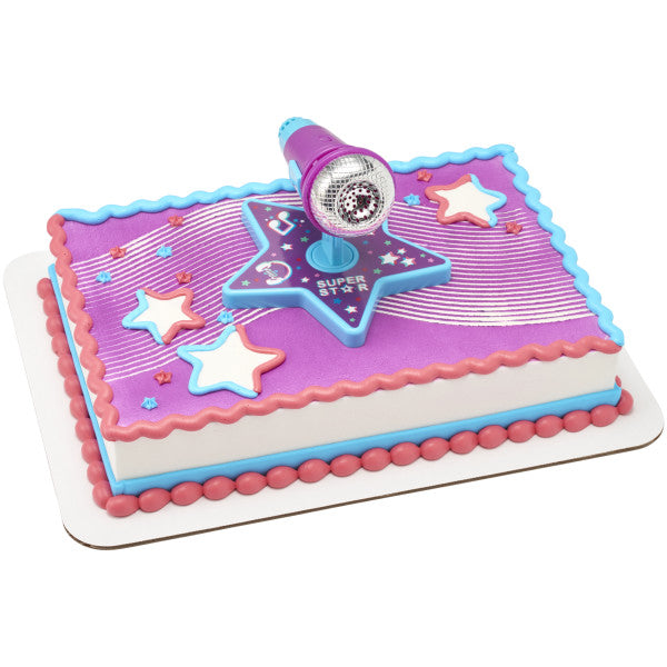 A rectangular cake decorated with pink, blue, and purple frosting, topped with the Super Star DecoSet microphone topper.