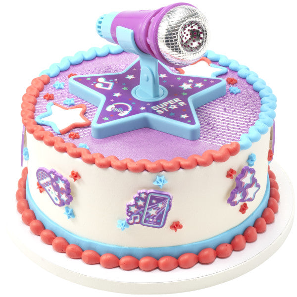 A round cake with music-themed decorations, bordered with blue and pink frosting, and featuring the Super Star DecoSet microphone topper.