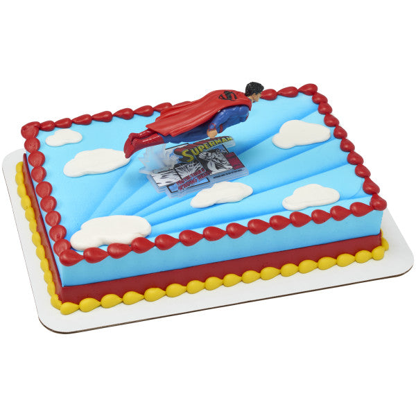 Rectangular cake decorated with blue icing, red and yellow borders, white fondant clouds, and a flying Superman figurine cake topper.