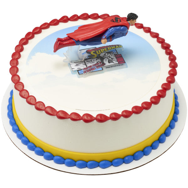 Round cake topped with flying Superman figurine and colorful red, yellow, and blue icing borders.