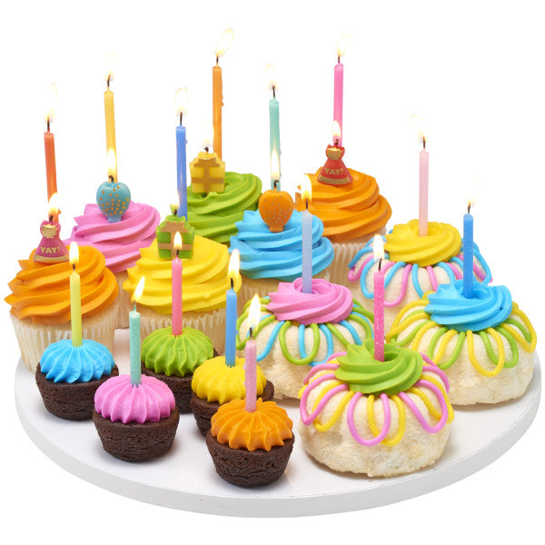 ssorted cupcakes, mini cupcakes, and frosted treats on a white platter topped with lit tall birthday candles in multiple bright colors, with colorful buttercream swirls.