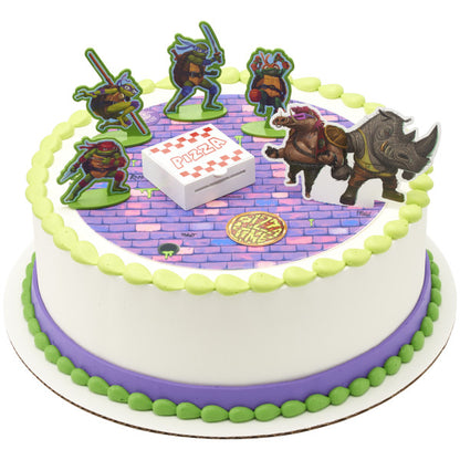 A round cake featuring the TMNT Pizza Power! DecoSet®, complete with a brick-patterned background and pizza launcher.