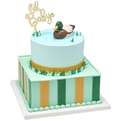 A two-tier cake with green and gold accents, topped with a duck decoy and "Oh Baby" sign.