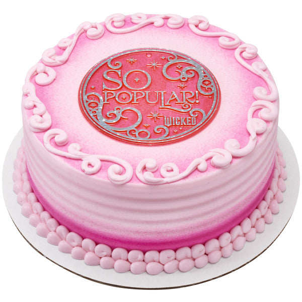 Pink ombré round cake with piped swirls and bead border, topped with the bright pink circular “SO POPULAR” Wicked plaque.