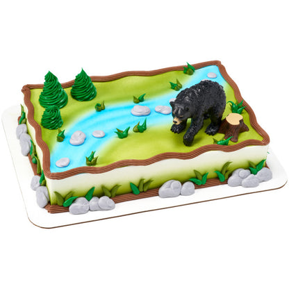 A nature-inspired cake featuring a river, trees, and the black bear topper.