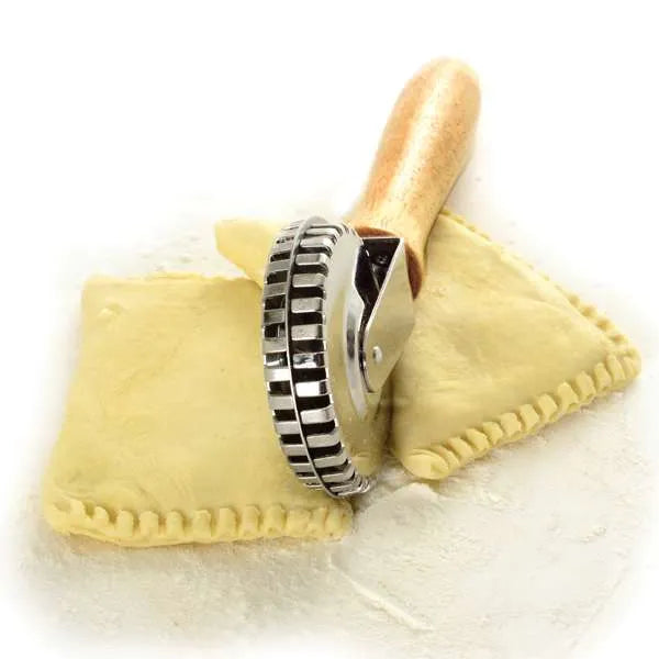 Wooden-handled pastry wheel being used to cut dough around two pieces of ravioli.