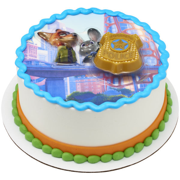 Round celebration cake with blue scalloped icing border and Zootopia-themed topper on top, featuring a gold police badge and character tray over a cityscape background.