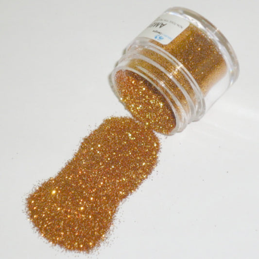 Clear plastic jar tipped on its side with fine American Gold glitter dust spilling across a white surface in a warm, sparkling golden trail.