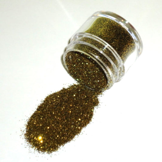 Clear plastic jar tipped on its side, spilling antique gold glitter dust with fine shimmering particles onto a white surface.