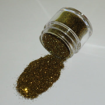 Small jar of gold non-edible galaxy glitter dust spilling onto a white surface.