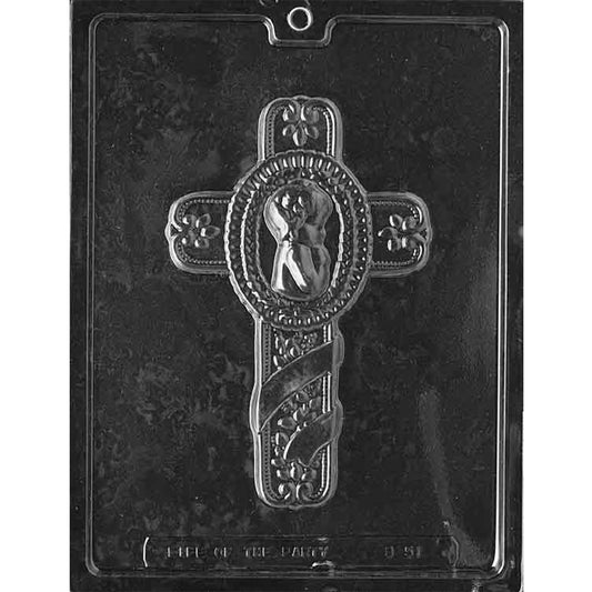 Clear plastic chocolate mold photographed on a dark background with one large cross-shaped cavity featuring a child cameo in the center, floral accents on the arms, and a ribbon motif across the lower section.