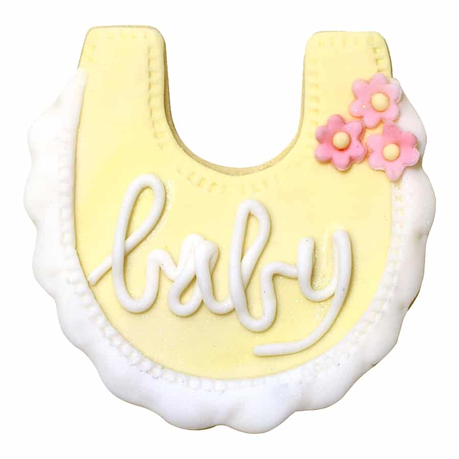 Decorated baby bib cookie with pastel yellow icing, white piping, and pink flower details.