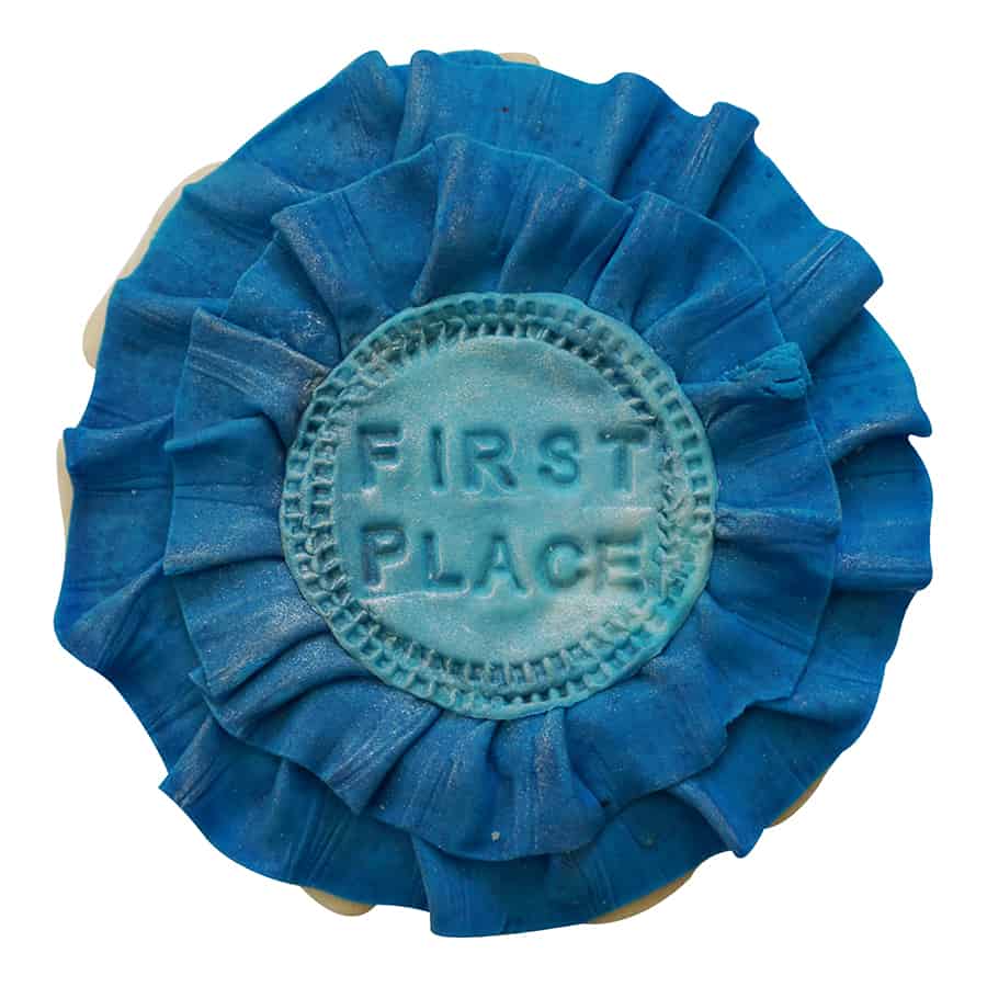 Decorated cookie shaped like a blue first place ribbon with layered fondant and stamped center