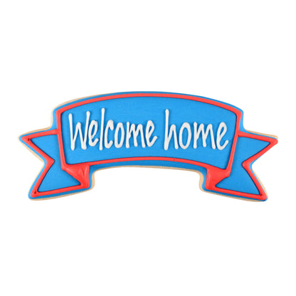 Decorated cookie shaped like a banner with 'Welcome Home' written in blue and red icing.