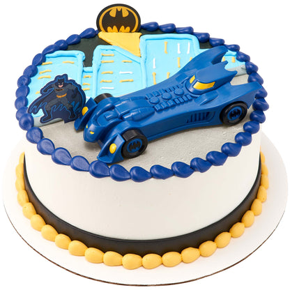 Round Batman cake topped with a large blue free-wheeling Batmobile, Batman figure, Bat-Signal emblem, blue city skyline, and yellow and navy frosting borders.