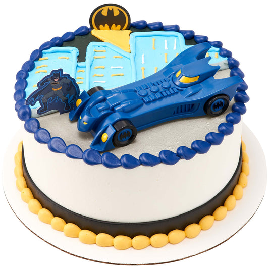 Round Batman cake topped with a large blue free-wheeling Batmobile, Batman figure, Bat-Signal emblem, blue city skyline, and yellow and navy frosting borders.