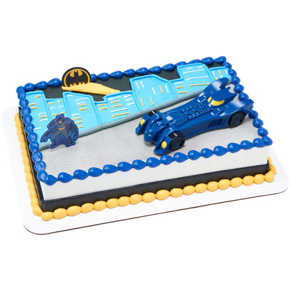 Rectangular Batman birthday cake decorated with a blue Batmobile, Batman figure, Bat-Signal emblem, and blue city skyline piping in blue, yellow, black, and gray.