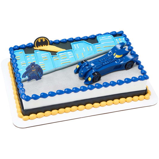Rectangular Batman birthday cake decorated with a blue Batmobile, Batman figure, Bat-Signal emblem, and blue city skyline piping in blue, yellow, black, and gray.