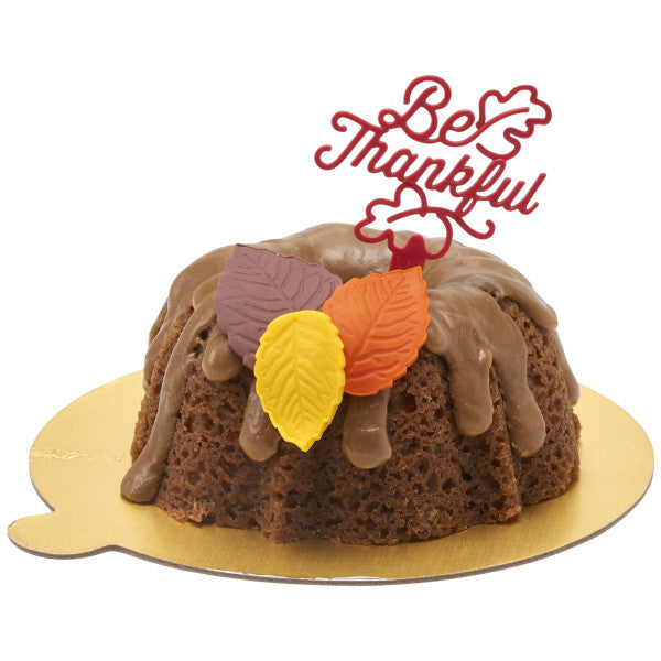 Mini bundt cake with chocolate glaze and leaf decorations, topped with a red “Be Thankful” pick.
