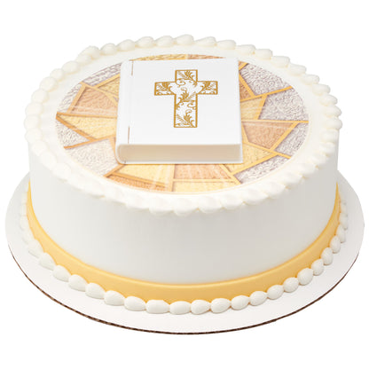 White Bible cake topper displayed on a round religious celebration cake with a gold-and-ivory edible image and white icing borders.