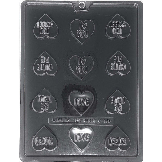 Clear Bite Size Heart Sayings Chocolate Mold photographed against a black background, showing 12 heart-shaped cavities with raised romantic sayings including I Love You, Love, Too Sweet, Cutie Pie, Be True, and XOXO.