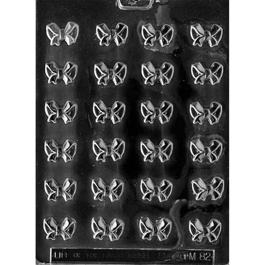 Clear plastic chocolate mold with 24 small bow-shaped cavities arranged in rows, designed for making bite-sized bow chocolates for decorating desserts.
