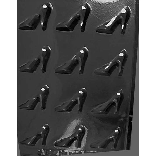 Clear plastic chocolate mold photographed on a dark background with multiple miniature high heel pump cavities arranged in rows, each showing a pointed toe and tall heel.